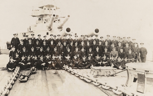 Black and white photograph of the officers and midshipmen of HMS Lion including Prince Louis Francis of Battenberg (later Lord Mountbatten), 1916 [MB2/A12/65]. He can be seen in the uniform of a midshipman, seated cross-legged in the middle of the front row, tenth from the left. He is holding a small dog, probably the ship's mascot.